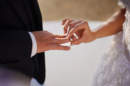without faces. The bride puts the wedding ring on the grooms finger.