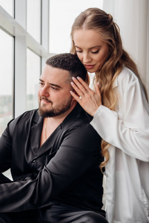 A gentle and romantic man and woman in silk pajamas on the windowsillの写真素材
