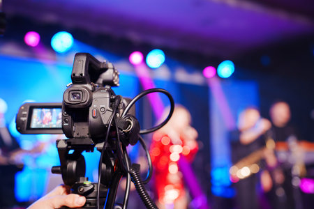 A professional videographer is filming a concert on stage. blurred artists on stage, focus on the...