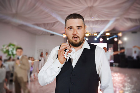 A groom with a beard in a vest throws the garter of the bride to his friends.