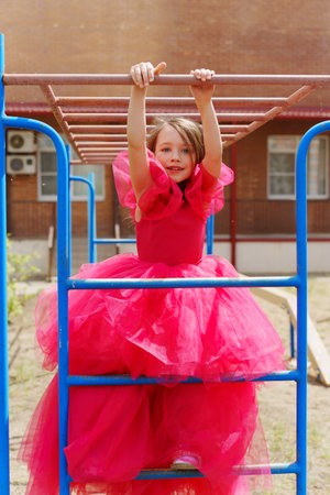 A cute little girl in an elegant lush pink dress is playing on the sports ground