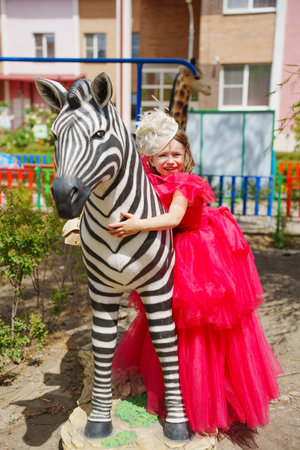 A girl in an lush pink dress is playing on the playground with animal sculpturesの写真素材