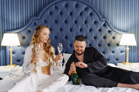 A man and a woman in silk pajamas with champagne are lying on a bed.の写真素材