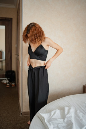 Woman adjusts her black pants in a hotel room before going outの写真素材