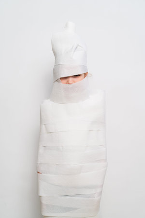 Person wrapped in strips of white material in a plain spaceの写真素材