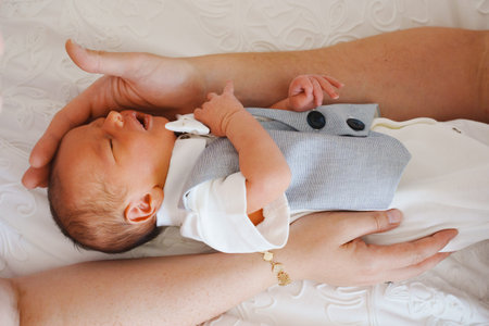 Baby dressed in suit lies on adults lap in soft light