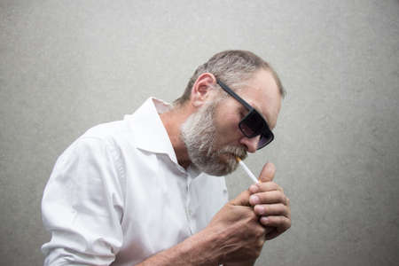 A man in a shirt with a beard in glasses smokes a cigarette