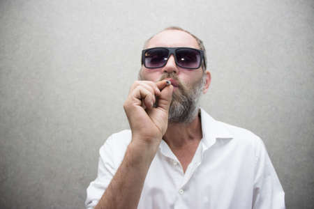 A man in a shirt with a beard in glasses smokes a cigarette