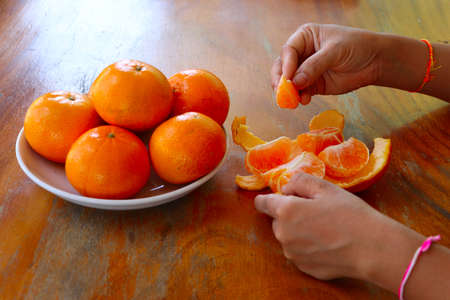Hands peeling ripe orange or tangerine fruit