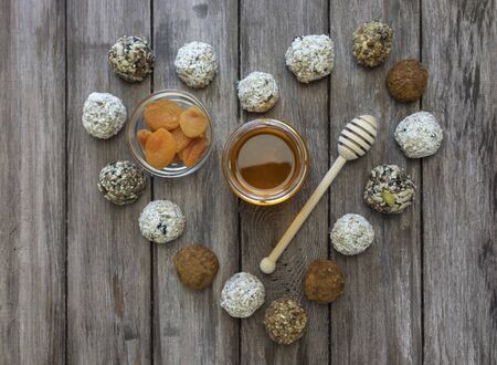 Energy balls or protein bars of oatmeal, honey, dried apricots and banana nuts on a wooden background in the shape of a heart, in the center of a jar of honey and dried apricots, flat layの写真素材