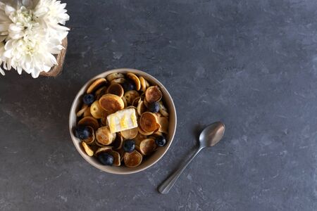 Fast breakfast, tiny pancakes, pancakes with berries and butter, breakfast concept, white flowers and a bowl with small pancakes, top viewの写真素材