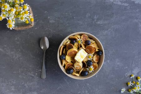 The plate is filled with tiny pancakes, the concept of a trendy breakfast, small pancakes with berries and honey and small daisies in the background, flat layの写真素材