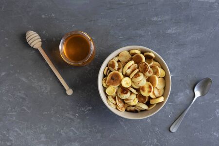 Breakfast concept, pancake porridge, tiny pancakes in a bowl and honey on a gray background, flat lay, Tiny pancake cerealの写真素材