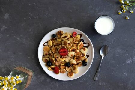 quarantine breakfast, homemade tiny pancakes with berries and honey, a glass of milk and chamomile in the background, trend 2020の写真素材