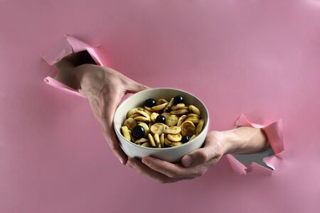 Men's hands hold a bowl of Tiny pancake cereal and berries through a hole in a paper wall, trend 2020の写真素材