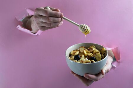 hands pour tiny pancakes with honey through holes in a paper wall, fast trendy breakfast 2020の写真素材