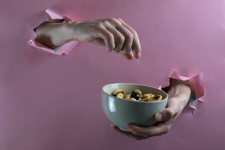 male hands take a berry from a bowl with tiny pancakes through holes in a paper wall, horizontal orientationの写真素材