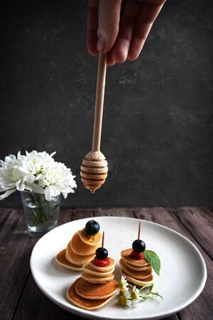 tiny pancakes on sticks with berries, a woman's hand pouring honey on tiny pancakes, trend food 2020の写真素材
