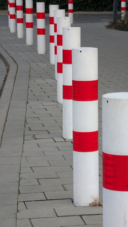 Red and white bollards in city. A series of red and white bollards line the sidewalk in an urban area, creating a clear barrier. The setting appears orderly and well-maintained.の写真素材