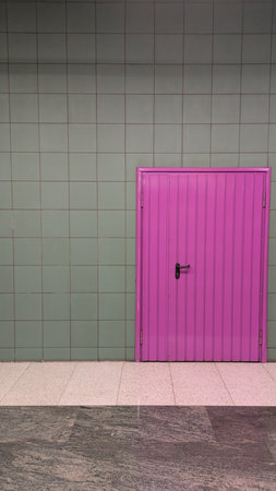 Pink Door in Tiled Urban Wall. A vibrant pink door set in a tiled wall creates a striking color contrast, reflecting urban design and modern street aesthetics.の写真素材