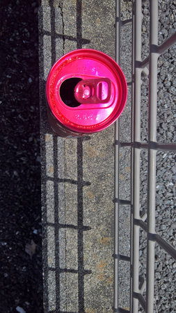 Bright Pink Aluminum Can on Concrete Curb. Open bright pink aluminum can be placed on a gray concrete curb near a metal fence, casting sharp shadows.の写真素材