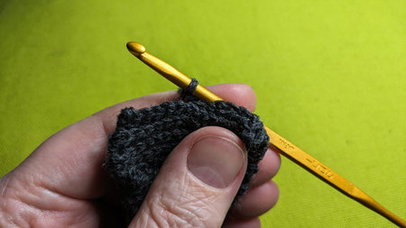 Hand crocheting with dark yarn and a golden hook against a green backgroundの写真素材