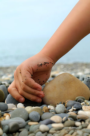 A child's hand plays with pebbles on the seashoreの写真素材