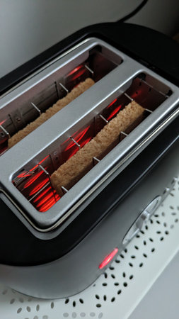 Bread Toasting with Red Heating Coils. Slice of bread toasting inside a toaster with glowing red...