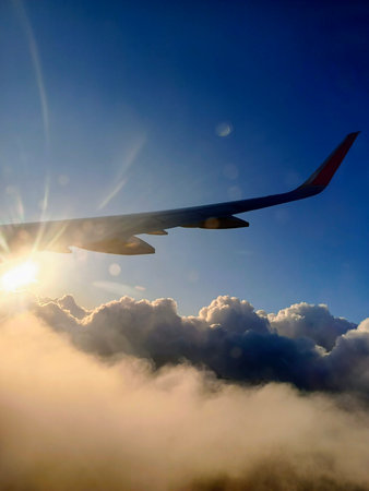 Airplane flying in the blue sky with clouds and sunbeamsの写真素材