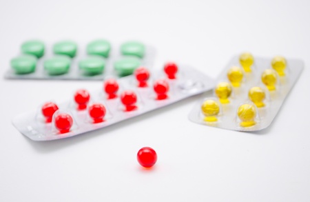 Round red pill and many different pills on a back background