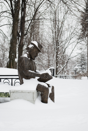 The sculpture "the man reads the book" in city park in the winter, under snowの写真素材