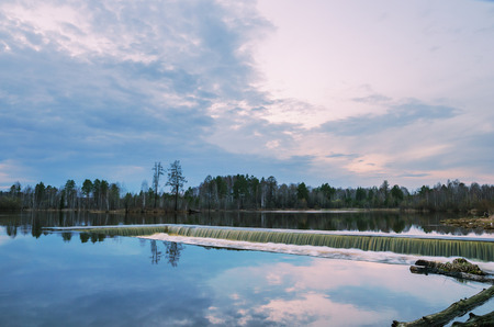 Unusual evening landscape with a dam, built on forest lakeの写真素材