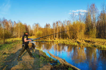 A fisherman catches a fish standing on the Bank of a small river in the rays of the setting sunの写真素材
