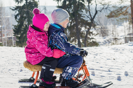 Children ride on a snow scooter on a bright Sunny winter dayの写真素材
