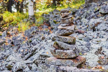 Pyramid of stones on the mountainside against the background of an autumn forest in the sunny day