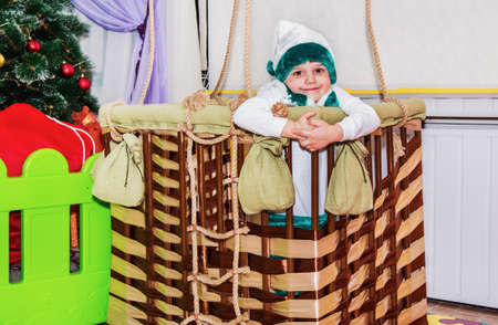 The boy is sitting in the basket of a balloon layout, he looks into the camera and smilesの写真素材