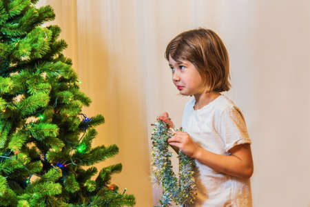 A little girl dresses up a Christmas tree, she decorates it with tinseの写真素材
