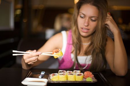 closeup portrait of girl with sushi in dark restaurant interiorの写真素材