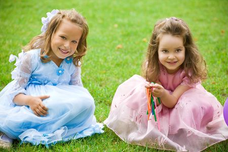 two little girls are sitting and playing on green grass