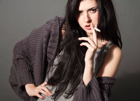 portrait of smoking young woman with cigarette on grayの写真素材