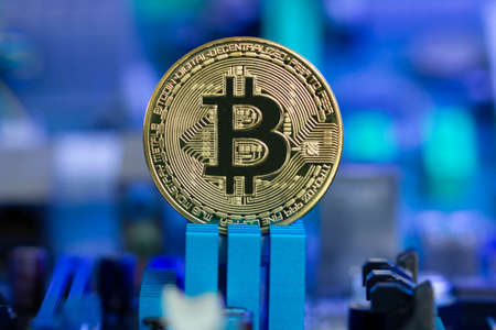 Golden Bitcoin coin on a blurred background of microchips and radio components in blue light. New...