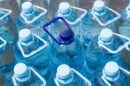 Many blue plastic bottles with blue caps and one with dark blue cap with clear mineral water in a supermarket. Pure filtered ecologically clean water in packaging. Close Up. One is different from allの写真素材