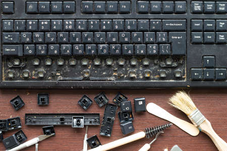 Old dirty computer keyboard with removed keys. The tools for repair and cleaning on the table in the...