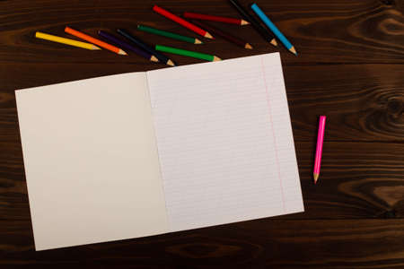 School notebook with oblique lines, colored pencils on the table wooden background. Blank sheet of paper in notebook on the desk. Back to school. School supplies. Top view. Copy space for textの写真素材