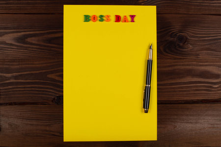 National Happy Boss Day. Multicolored colorful letters in a yellow blank page with pen on the table. Bosses day office greeting card with copy space for text. Close-Up. Top view. View from aboveの写真素材