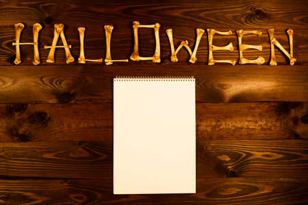 Lettering from the bones of the word Halloween and blank sheet of paper on a dark brown wooden...