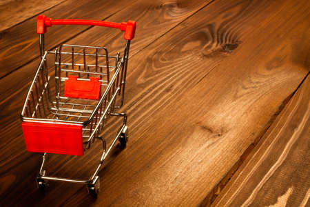 Black Friday concept. Shopping cart on the table. Metal shopping cart with wheels on a brown wooden background. Ready to shopping. Ecommerce online shopping discount ads. Copy space for text. Close-upの写真素材