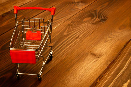 Black Friday concept. Shopping cart on the table. Metal shopping cart with wheels on a brown wooden background. Ready to shopping. Ecommerce online shopping discount ads. Copy space for text. Close-upの写真素材
