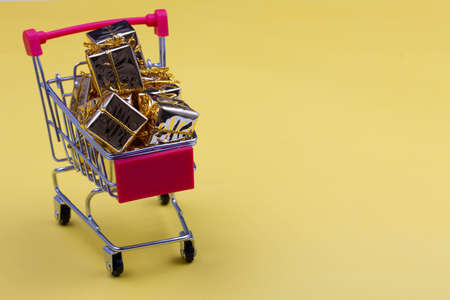 Black Friday concept. Shopping cart on the table. Metal shopping cart with wheels on a yellow...