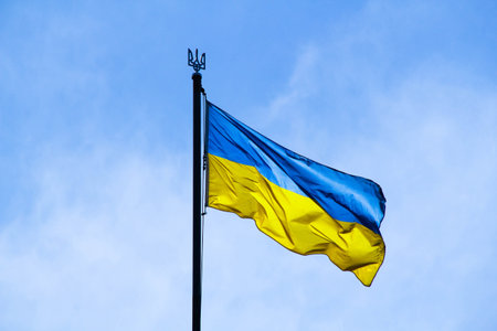 Ukrainian flag in the rays of the rising sun on a background of sky. Bicolor blue and yellow national flag of Ukraine on a flagpole and coat of arms of Ukraine trident. Official symbol of Ukraineの写真素材